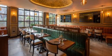 Elegant restaurant interior with green leather seating and wooden tables.