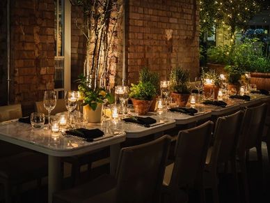 Elegant outdoor dinner table with candles and plants creating a cozy ambiance.
