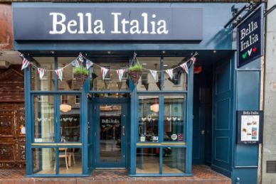 Front view of Bella Italia restaurant with decorative flags and hanging plants.