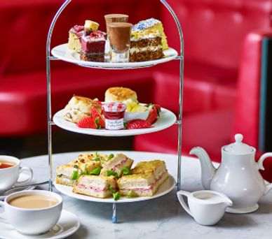 A three-tiered tray with assorted sandwiches, desserts, and tea set on a marble table.