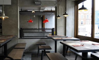 Industrial-style empty restaurant with wooden benches and red pendant lights.