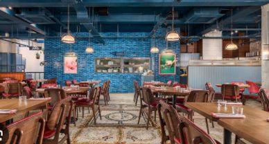 Spacious restaurant interior with wooden tables and blue brick wall.
