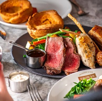 A plate with roast beef, Yorkshire pudding, vegetables, and gravy on a marble table.