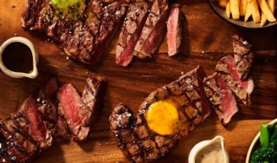 Grilled steaks with sauces and fries on a wooden board.