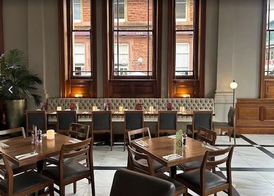 Elegant restaurant interior with wooden tables and tufted seating by large windows.