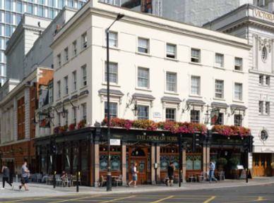 Historic pub with flower boxes on its balcony in a city setting.