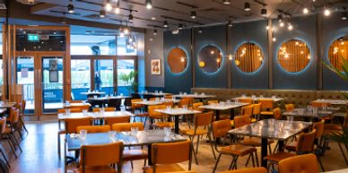 Modern restaurant interior with wooden tables and orange chairs.