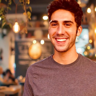 Young man with friendly smile, wine colored shirt and cafe backdrop
