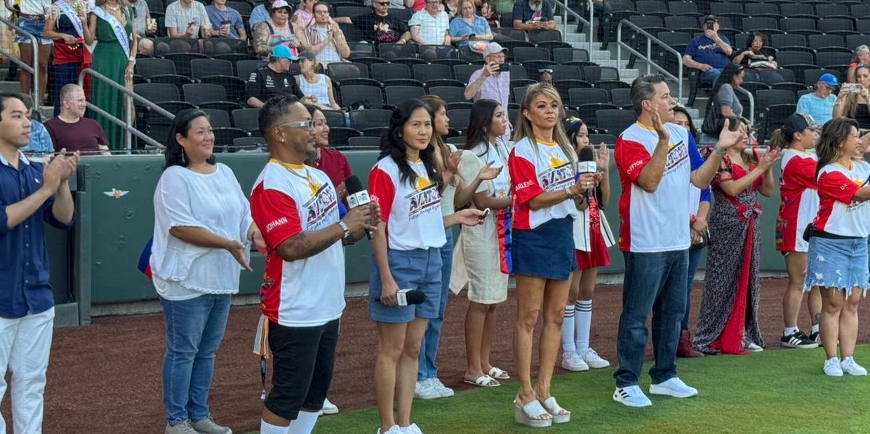 Group of people standing on a field, some holding microphones, others clapping at an event.