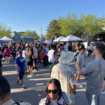 People gather outdoors at a lively event with tents and booths under clear blue skies.