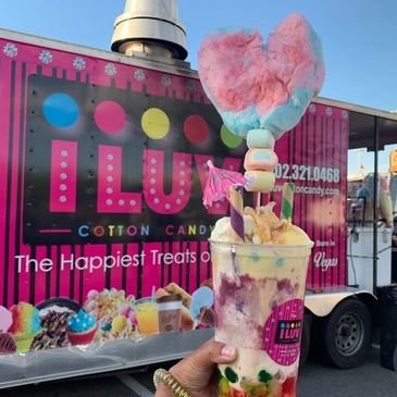 Colorful cotton candy treat held in front of a vibrant cotton candy truck.