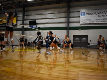 Female volleyball players intensely engaged in a match inside a gym.