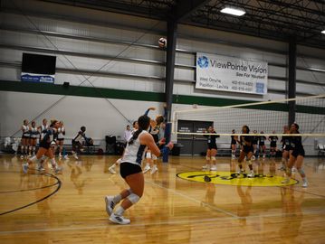 Two volleyball teams compete indoors with players ready for action near the net.