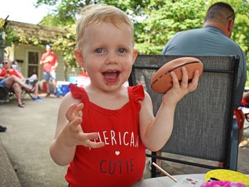 Happy toddler in a red outfit holding a small football outdoors.