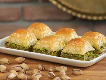 Close-up of pistachio baklava pieces on a white plate with pistachios scattered around.