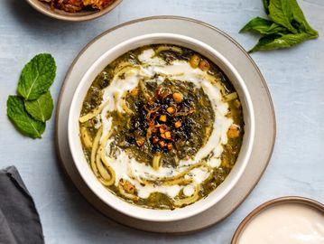 A bowl of creamy, green soup garnished with herbs and spices, served with fresh mint leaves.