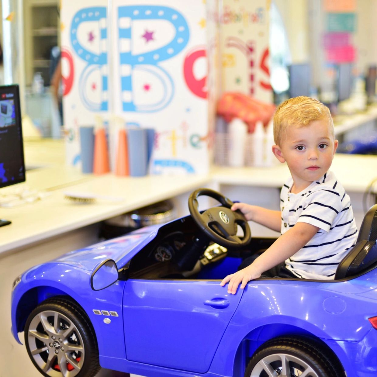 A boy sat in  a car chair at Bertie and Belle childrens hair salon. A place to get a kids cut