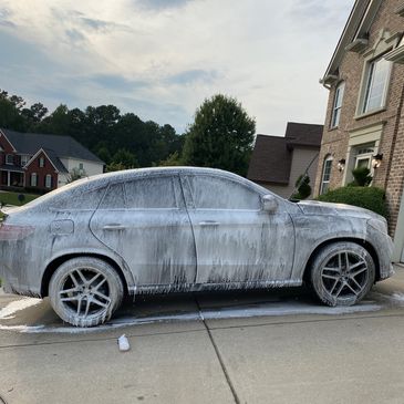  Mercedes Benz SUV covered in cleaning foam during a wash in a residential driveway.