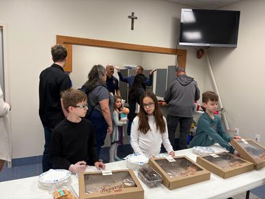 Children serving pastries at a community event with adults in the background.