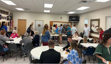 Community gathering in a hall with people socializing and eating.