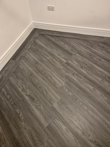 Close-up of gray wood-patterned flooring and white baseboards in a corner.