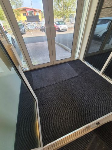 Entrance door area with black floor mats and glass panels.