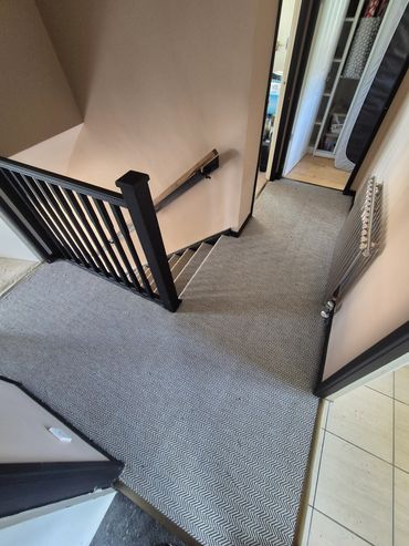 Carpeted hallway with stairs and open doors.