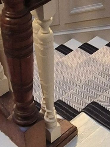 Close-up of contrasting wood and white balusters on a staircase with a patterned carpet.