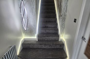 Modern staircase with soft LED lighting and grey carpet.