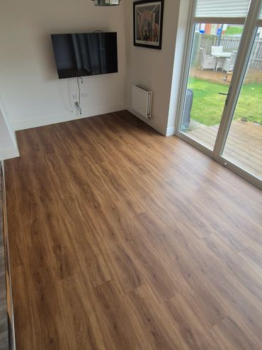 Modern room with wooden floor, wall-mounted TV, and garden view through glass door.