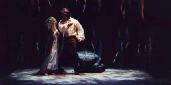 A man and woman in a dramatic, dimly lit stage scene.