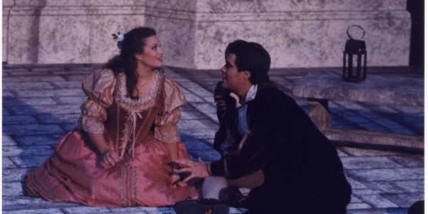 Two actors in period costumes perform a dramatic scene on stage.