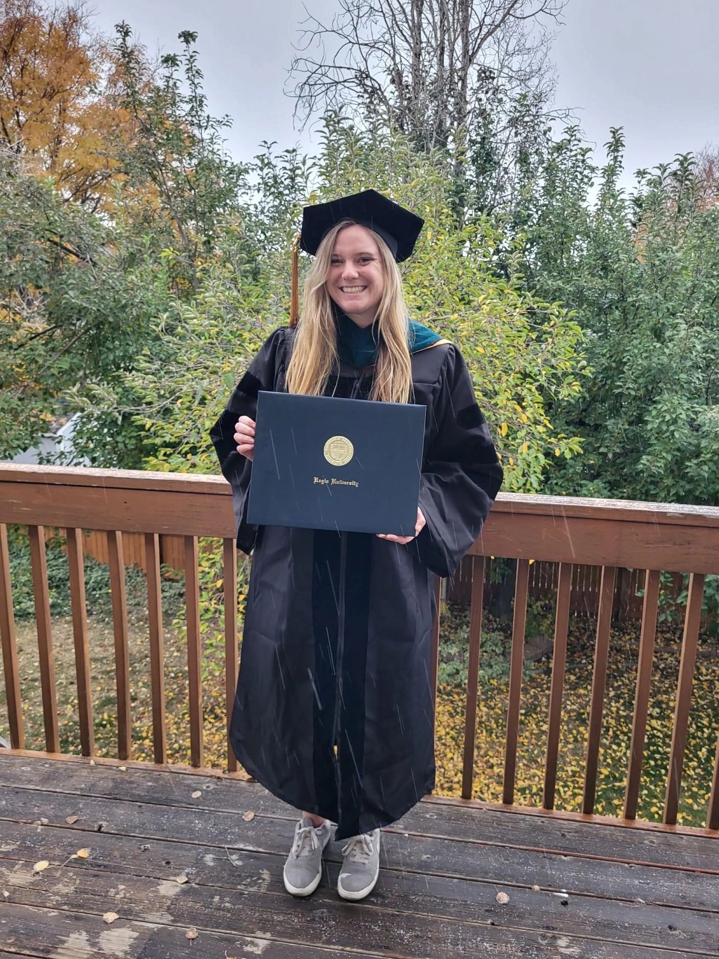 A smiling graduate in cap and gown holding a diploma outdoors.
