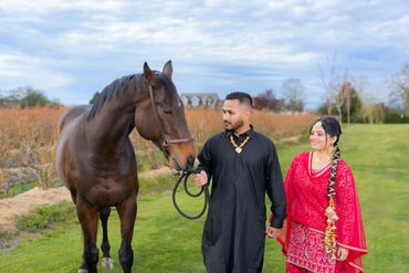 A couple in traditional attire walking a horse on a green field.
