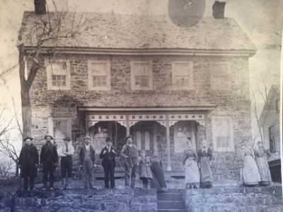 Black and white photo of people standing in front of a stone house.
