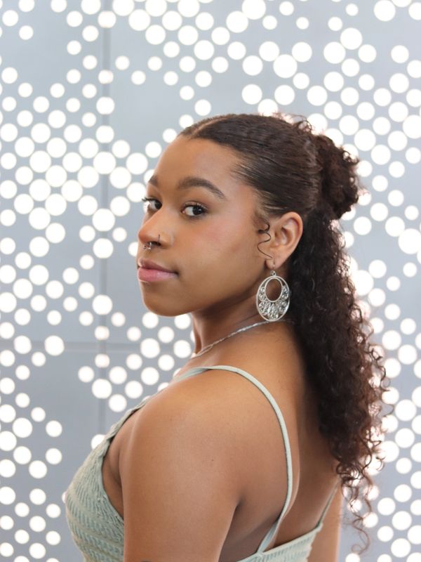 Woman with curly hair and hoop earrings against a dotted background.