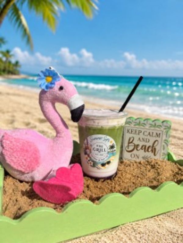 Pink flamingo toy with drink and beach sign on sandy shore.