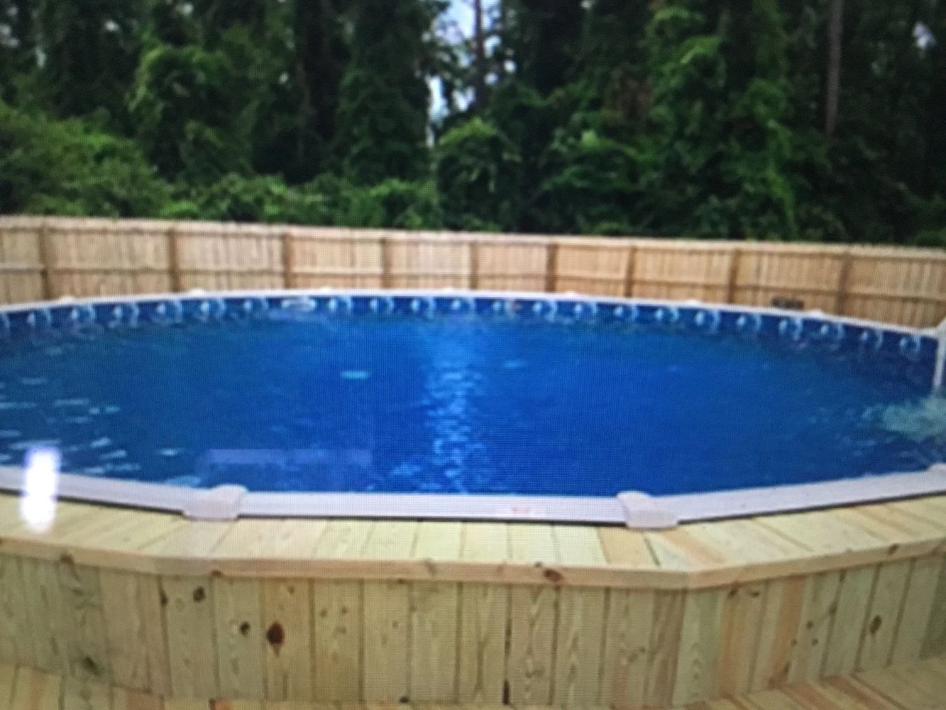 A round above-ground swimming pool with wooden decking and a privacy fence.