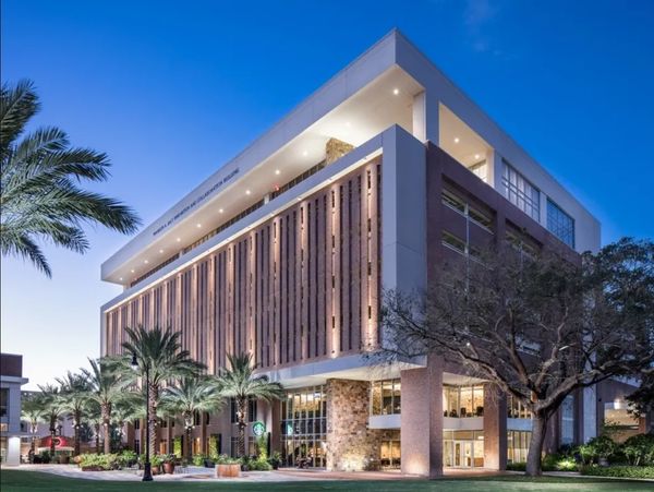 Modern multi-story building with palm trees at dusk.