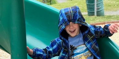Child smiling on a green slide wearing a blue jacket.