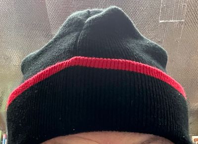 A person wearing a black beanie with a red stripe.