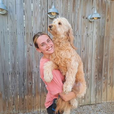 A woman happily holding a large fluffy dog in front of a wooden fence.
