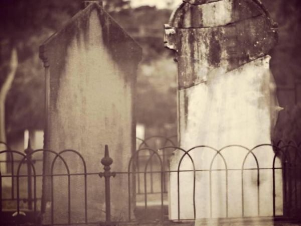 Two weathered tombstones behind an iron fence in a graveyard.