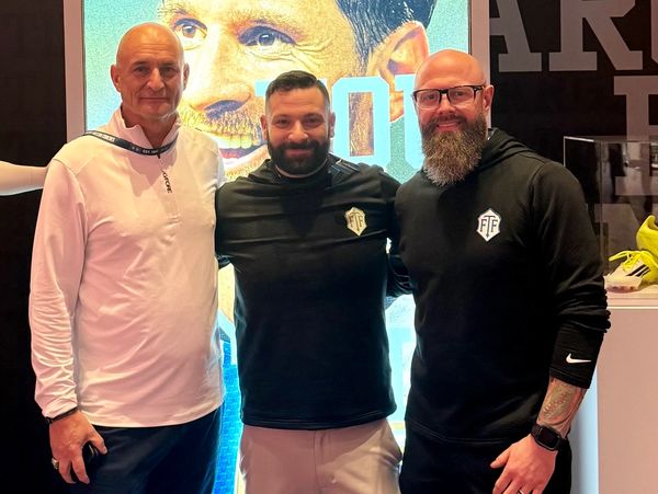 Three men posing together in casual sportswear with a large graphic backdrop behind them.