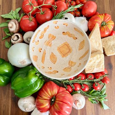 A ceramic pasta bowl styled with tomatos, peppers onions and cheese around the hand painted pasta bo