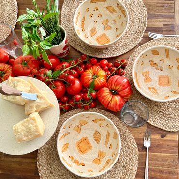A tablescape of 3 pasta bowls set ready to eat at with tomatos and cheese.
