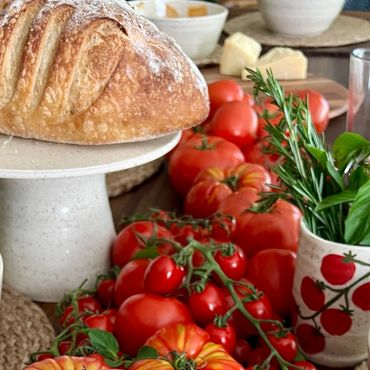 A photo of a handmade ceramic serving platter, with tomatos on the vine next to a painted tomato cup