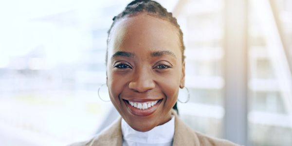 Smiling woman with braided hair and hoop earrings outdoors.