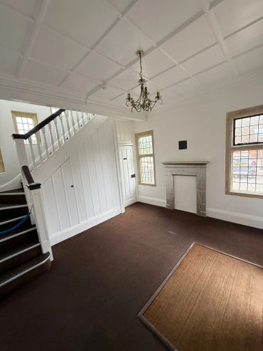 Empty room with staircase, chandelier, and fireplace under natural light.