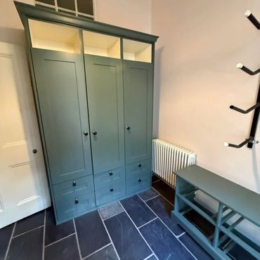A green wardrobe and shoe rack in a room with black tiled flooring.